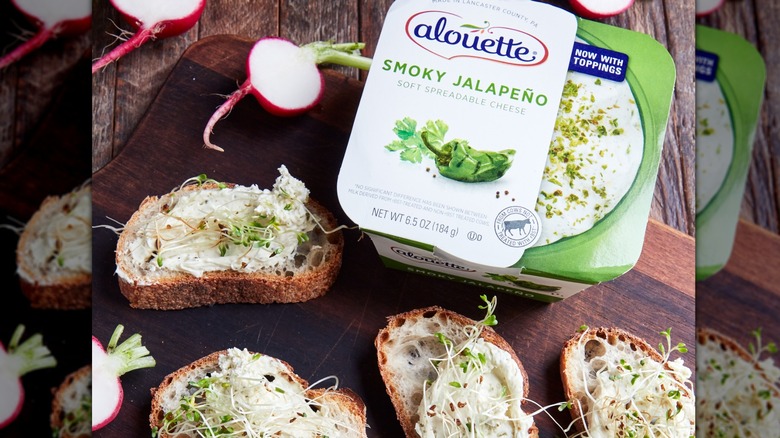 A package of Alouette smoky jalapeno cheese next to crostini with cheese and sprouts