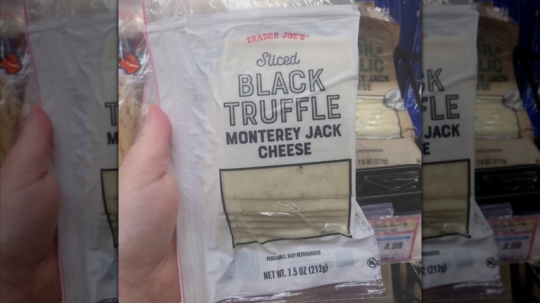 A person holding a package of sliced black truffle Monterey jack cheese at Trader Joe's