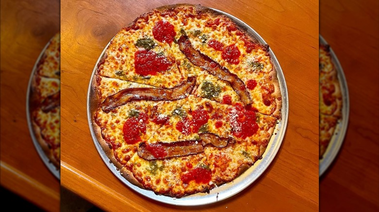 A pizza with bacon and tomatoes on a table