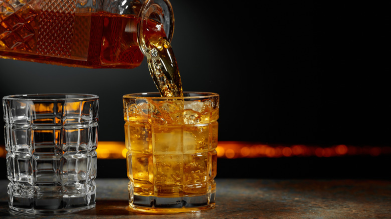 Whiskey is poured from a decanter into a glass with ice