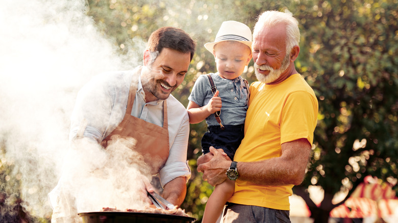 Grandpa, son, and young grandson grilling together outdoors