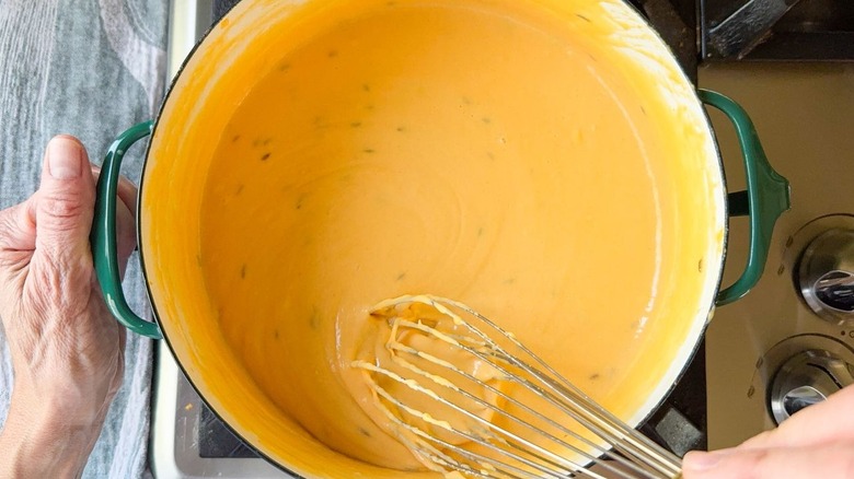 whisking beer cheese dip in large pot on stovetop