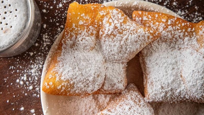 Close-up shot of three beignets with powdered sugar all over them and the table