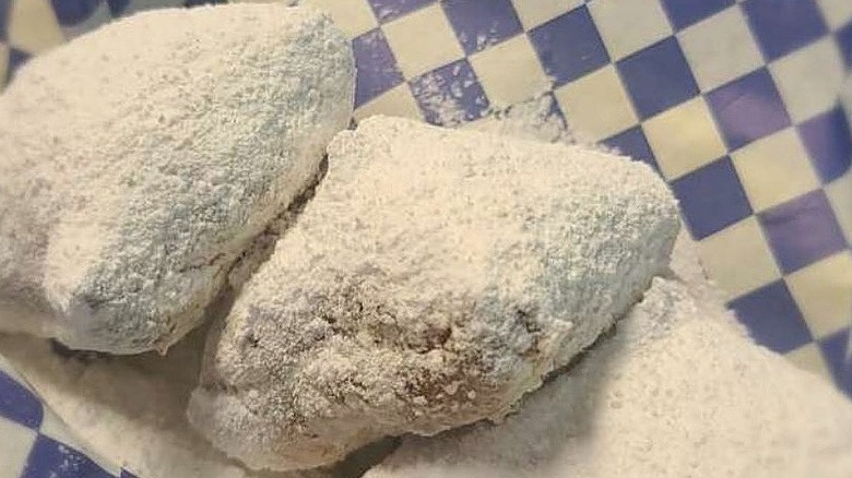 Three sugar-covered beignets arrayed in a line on a blue and white checked paper
