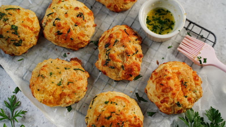 Buttermilk biscuits with butter and herbs on a wire rack are photographed from above.