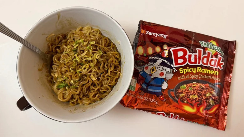 A package of Buldak's Yakisoba ramen noodles sit next to a white bowl filled with the same noodles