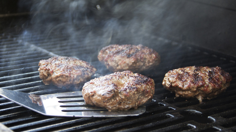 Hamburgers on the grill with stainless steel spatula under one.