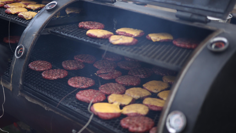 Burgers and cheeseburgers being cooked in an open smoker.