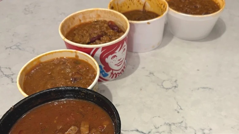Five different chain restaurant chilis lined up on a white countertop.