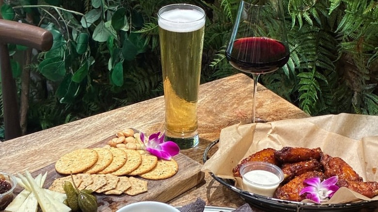 A charcuterie board on the left, beer and wine in the middle, and chicken wings on the right, all served on a table.
