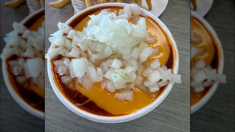 Overhead view of a cup of chili topped with cheese and diced white onions