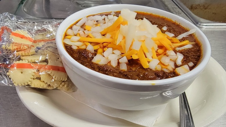 Bowl of chili with onions and cheese and package of oyster crackers