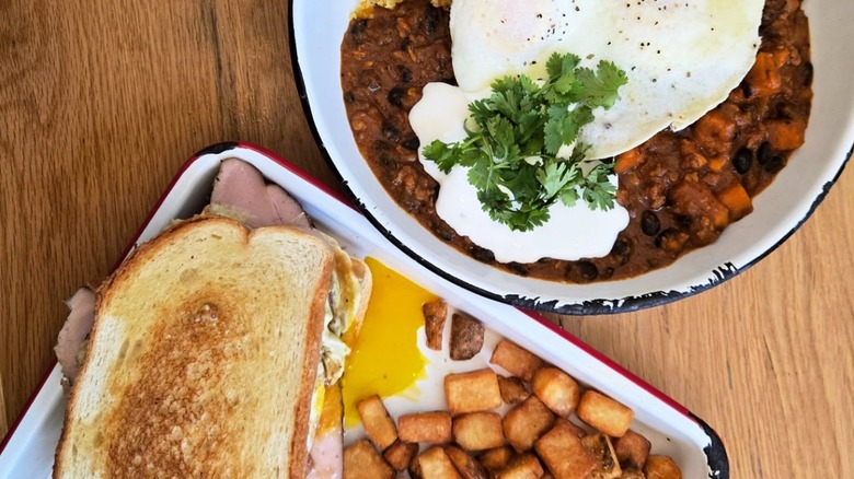 Bowl of chili with egg and tray of hash browns and sandwich