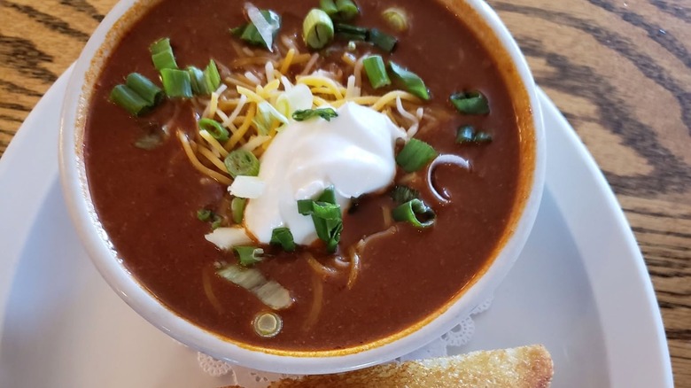 Bowl of chili with sour cream, onions, and cheese on plate
