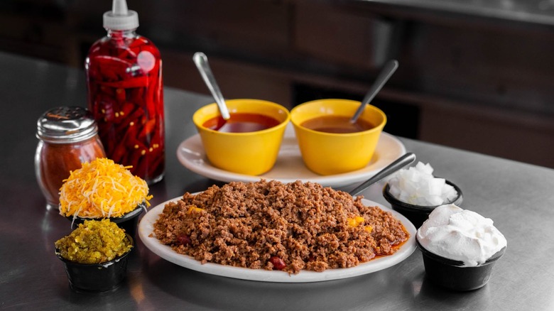 Plate of chili on counter with sides of cheese, onions, sour cream, sauces, and peppers
