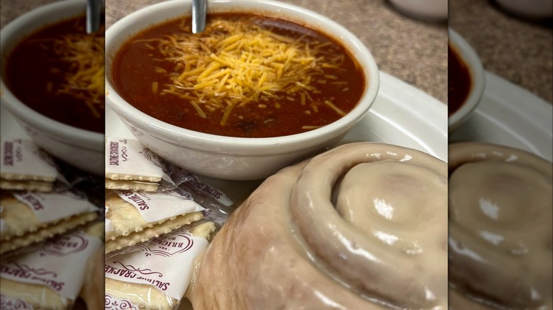 Bowl of chili with cinnamon roll and packages of crackers