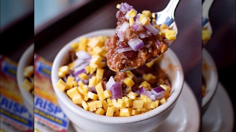 Chili with onions and cheese on a spoon with bowl