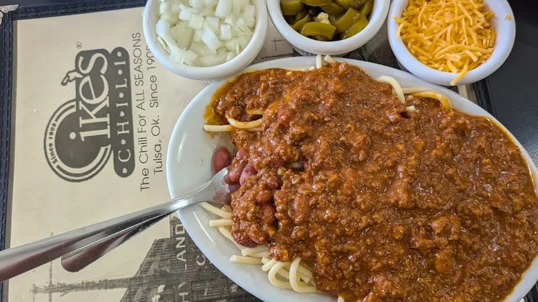 Plate of chili and spaghetti with side dishes of cheese, jalapeños, and onions with Ike's menu