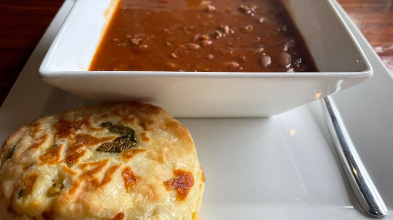 Square bowl of chili with jalapeño biscuit on plate