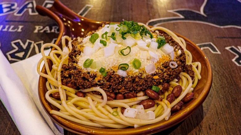 Bowl of chili with spaghetti, beans, and onions on table