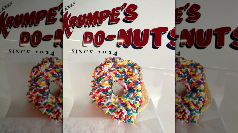 Donut with sprinkles in front of a sign for Krumpe's Do-Nuts