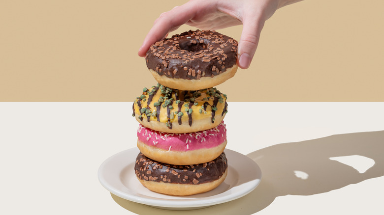 Stack of dontus on a plate, with a hand lifting the top donut off the stack