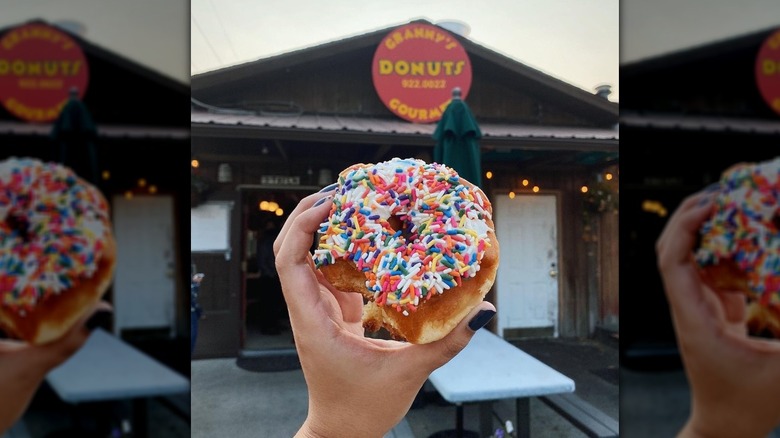 Hand holding a sprinkle donut in front of the storefront for Granny's Gourmet Donuts