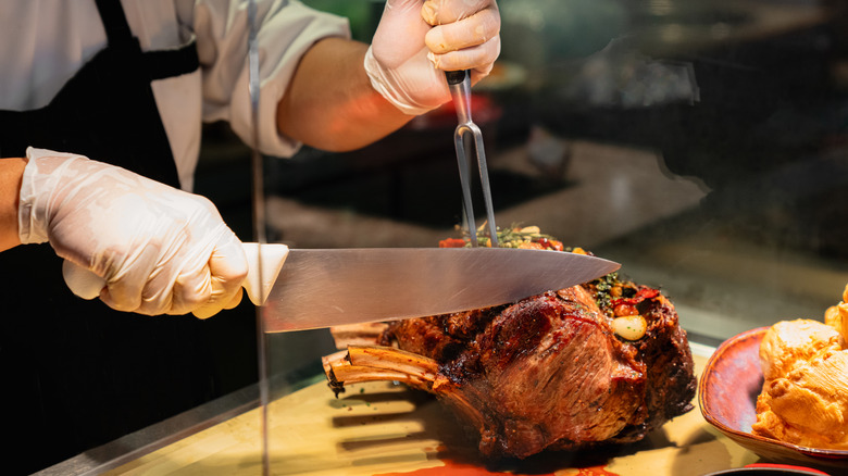 A chef cutting a prime rib roast with a large knife.