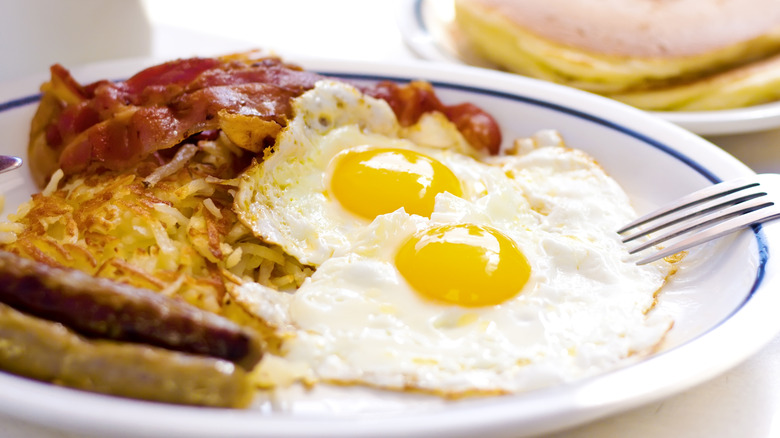 A plate of fried eggs, hash browns sausage, and bacon