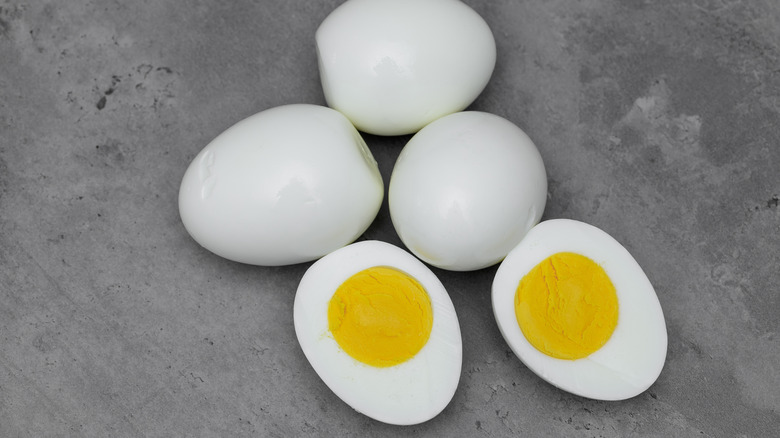 A halved, perfectly cooked hard-boiled egg with three other whole hard-boiled eggs over a gray table.