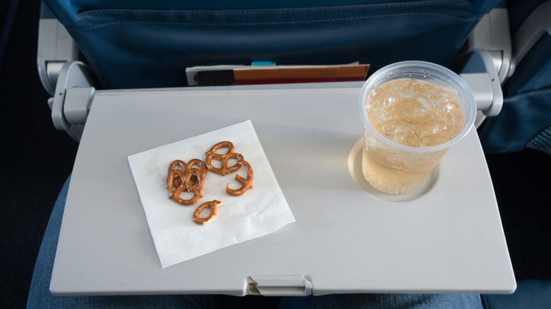 An illustrative image showing pretzels and a drink on a plane tray table.