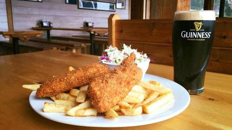 Breaded fried fish, chips, and coleslaw on plate beside pint of Guinness