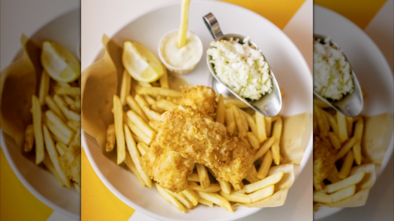 Fish and chips with coleslaw, tartar sauce, and lemon on white plate