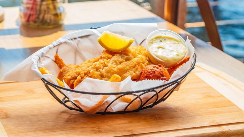 Basket of fried catfish with tartar sauce and lemon on wooden board