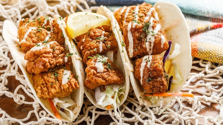 Three fried fish tacos with lemon on table