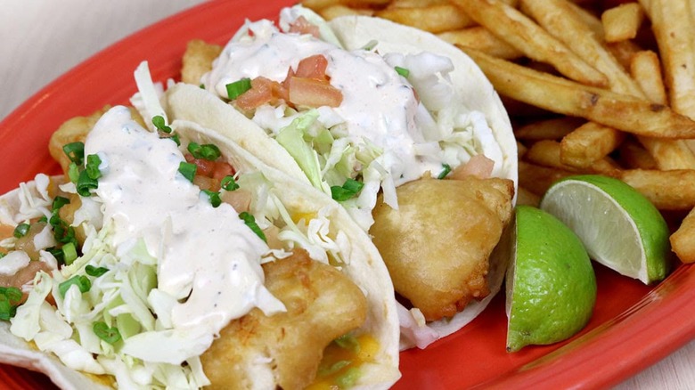 Two fried fish tacos with limes and fries on red plate