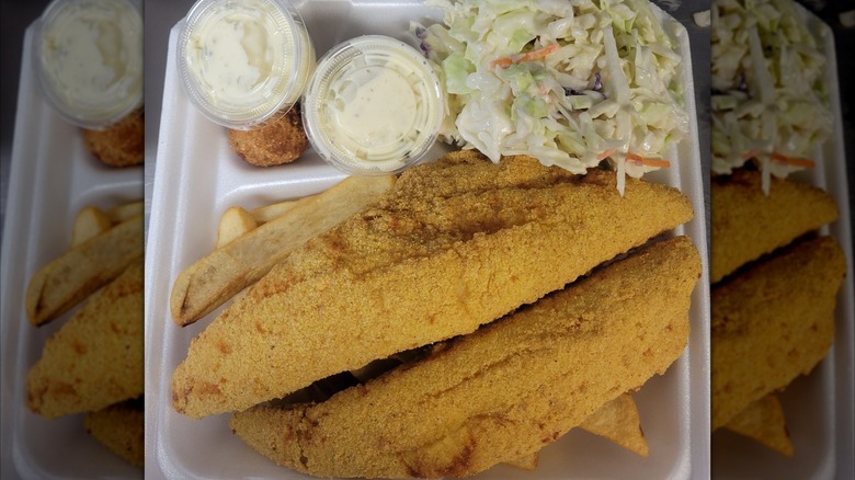 Fried fish filets in white tray with coleslaw and dip cups