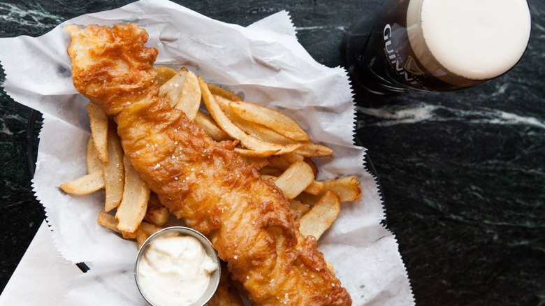 Fish and chips on paper beside pint of Guinness