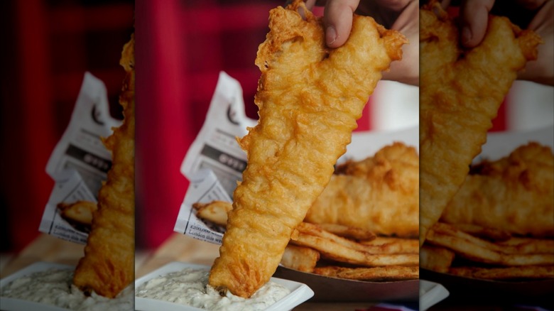 Hand holding piece of fried fish and dipping it in tartar sauce