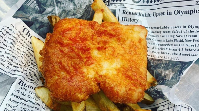Piece of fried fish with fries on newspaper