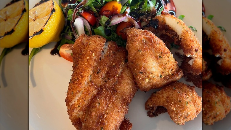 Pieces of fried fish on plate with dressed greens