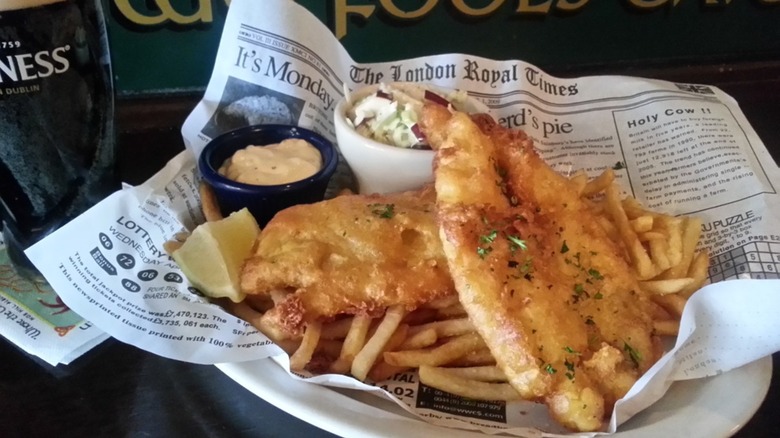 Fish and chips with coleslaw and tartar sauce on newspaper beside pint of Guinness