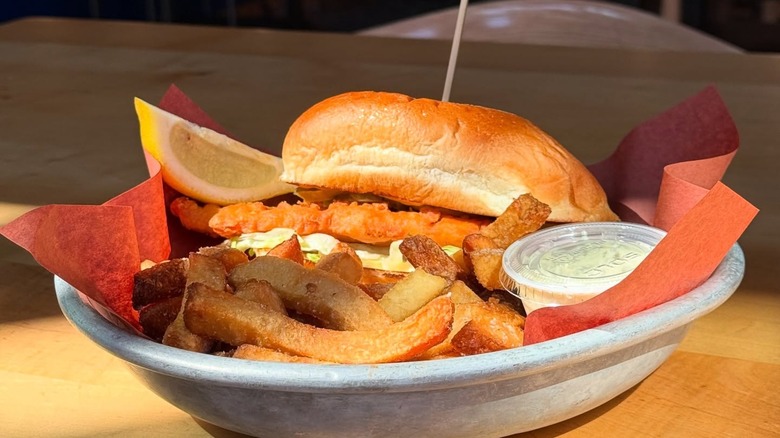 Fried fish sandwich with chips and lemon wedge on red paper