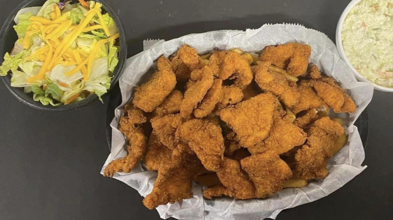 Basket of fried catfish pieces beside bowl of salad and coleslaw