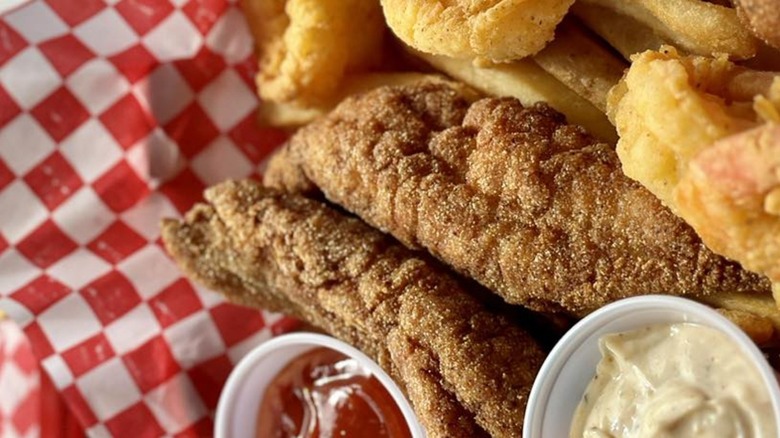 Fried catfish filets with ketchup and sauce on red and white paper