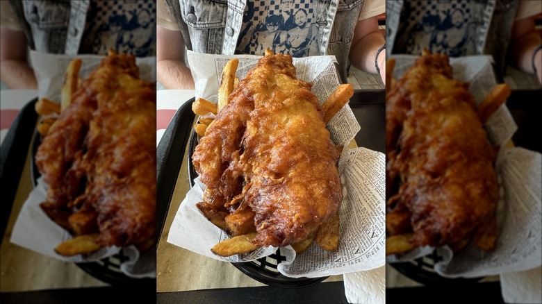 Piece of fried fish and chips in black, plastic basket