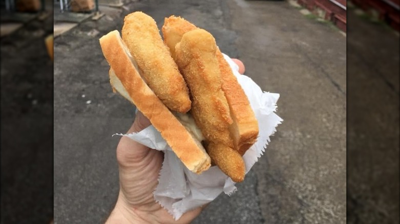Hand holding fried fish filet sandwich with pavement in background