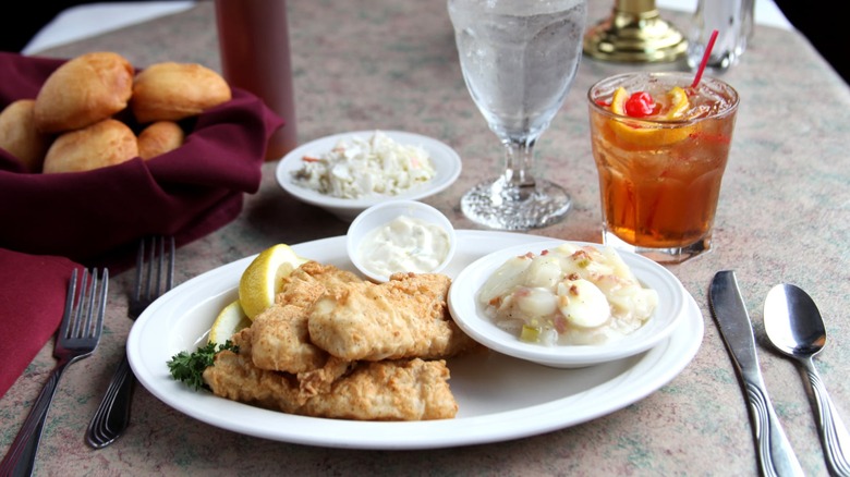 Fish fry on plate with potato salad, glass of water, and cocktail