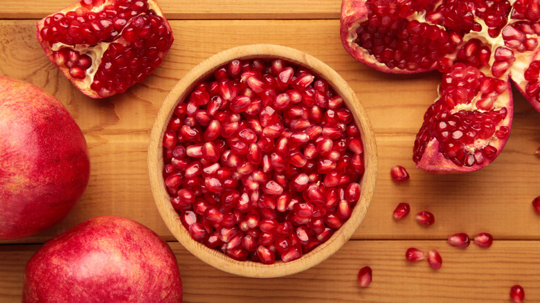 a bowl of pomegranate seeds with broken open pomegranates next to it