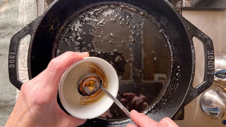 Using a ladle to remove bacon fat from cast iron skillet on stovetop